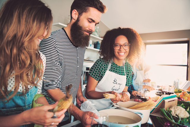 Drei Freunde internationaler Herkunft stehen zuhause in der Kueche und kochen gemeinsam.